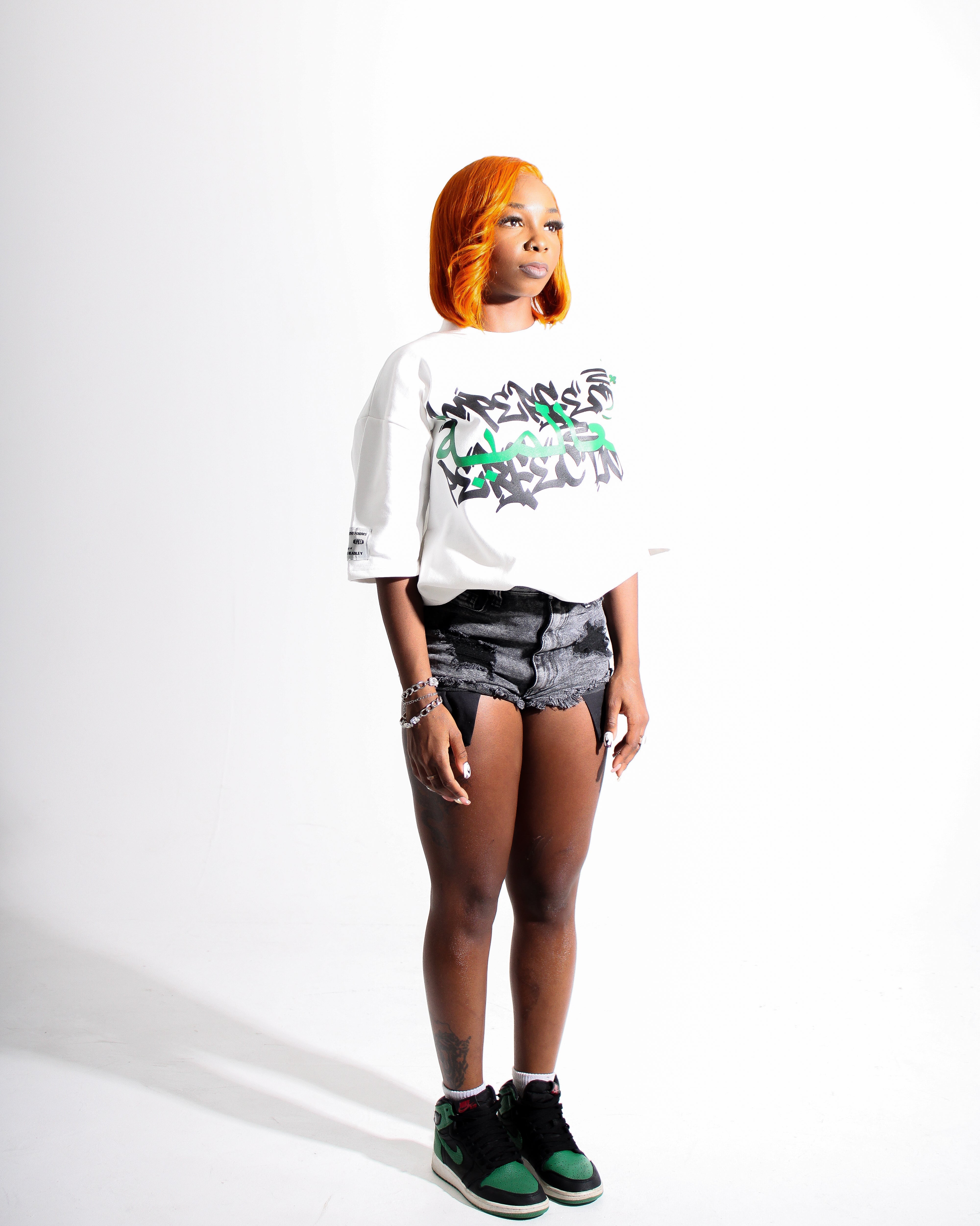 Person wearing a white sweatshirt with a graphic design, denim shorts, and green sneakers on a white background