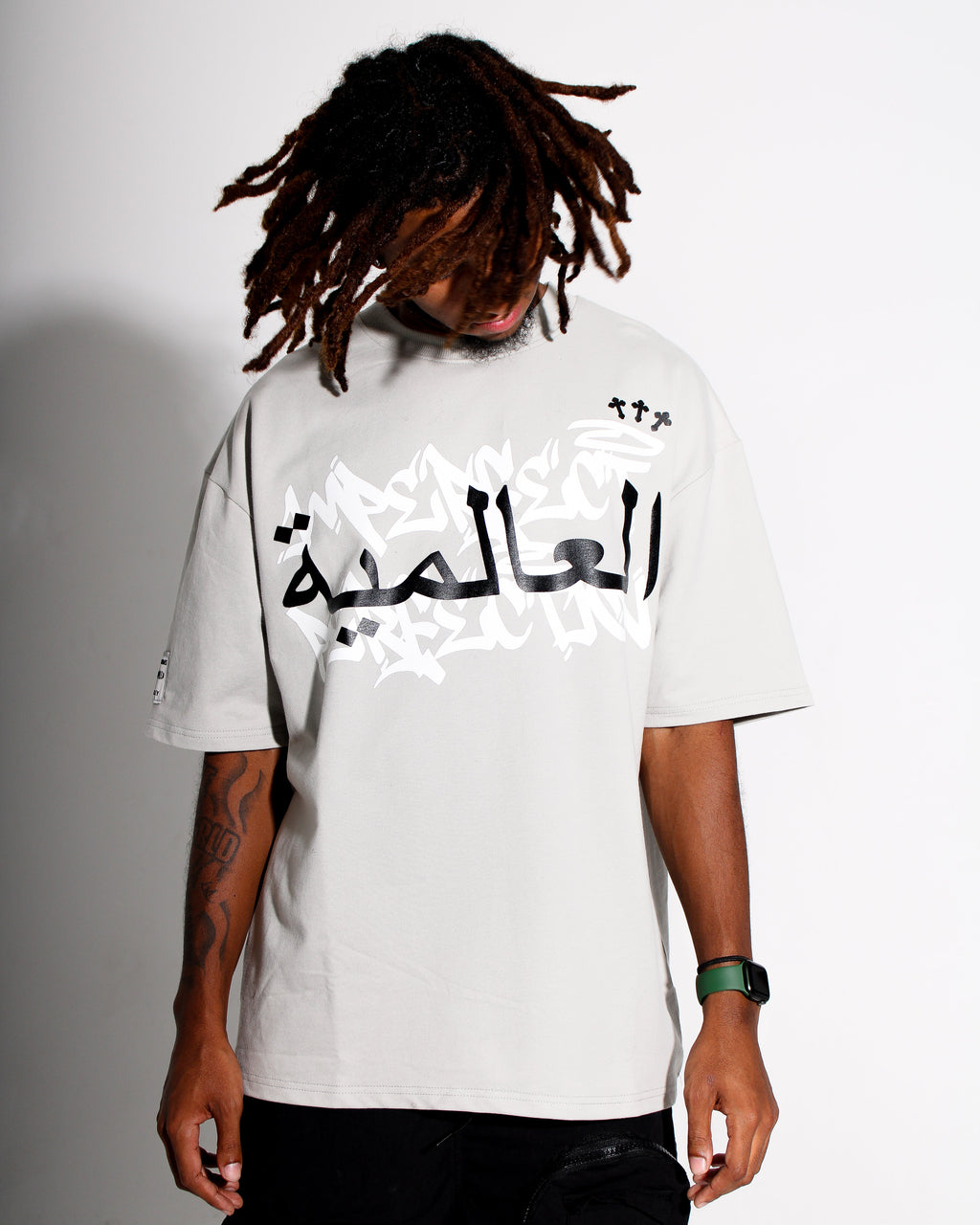 Person wearing a grey t-shirt with Arabic text on a plain background