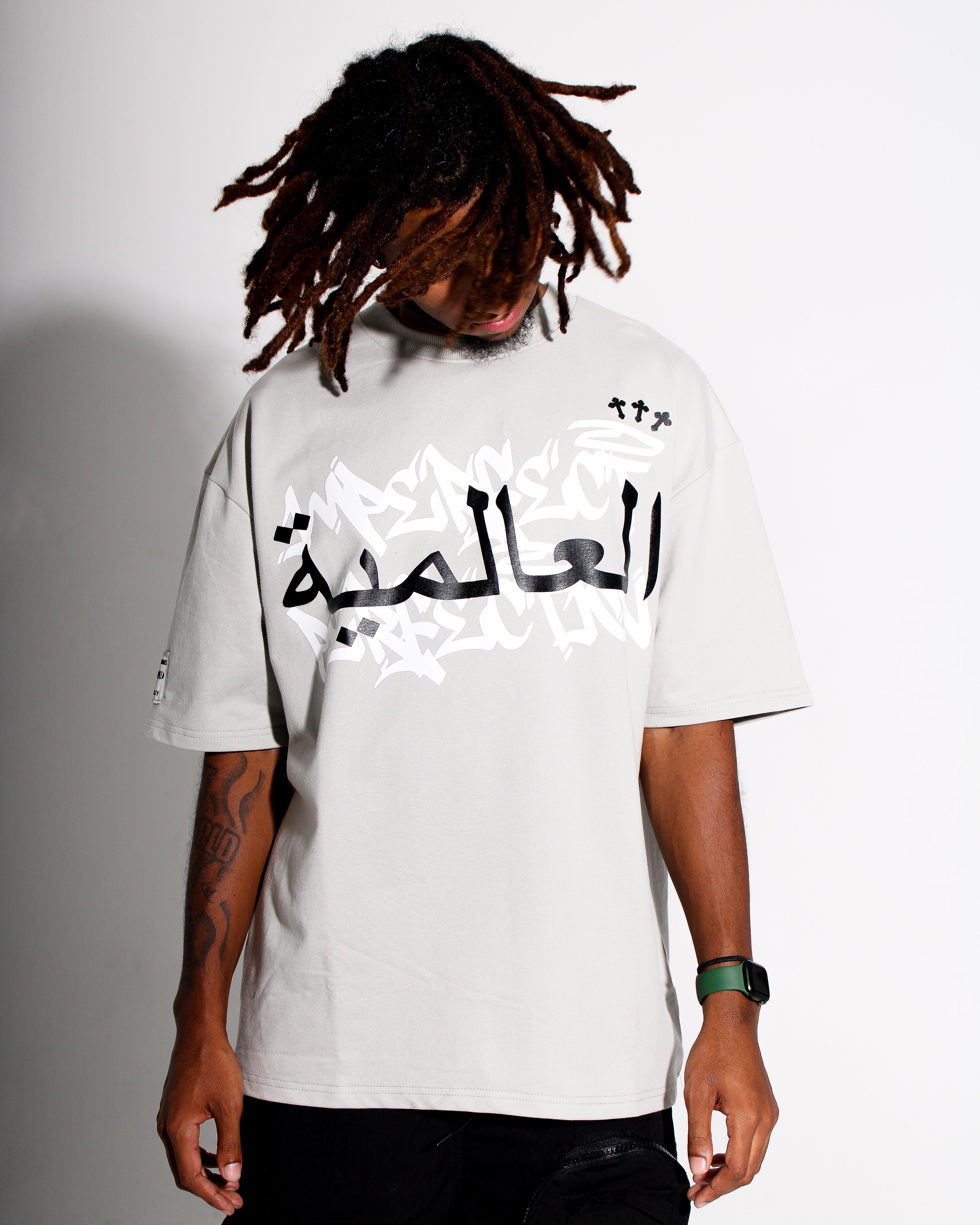 Person wearing a grey t-shirt with Arabic text on a plain background