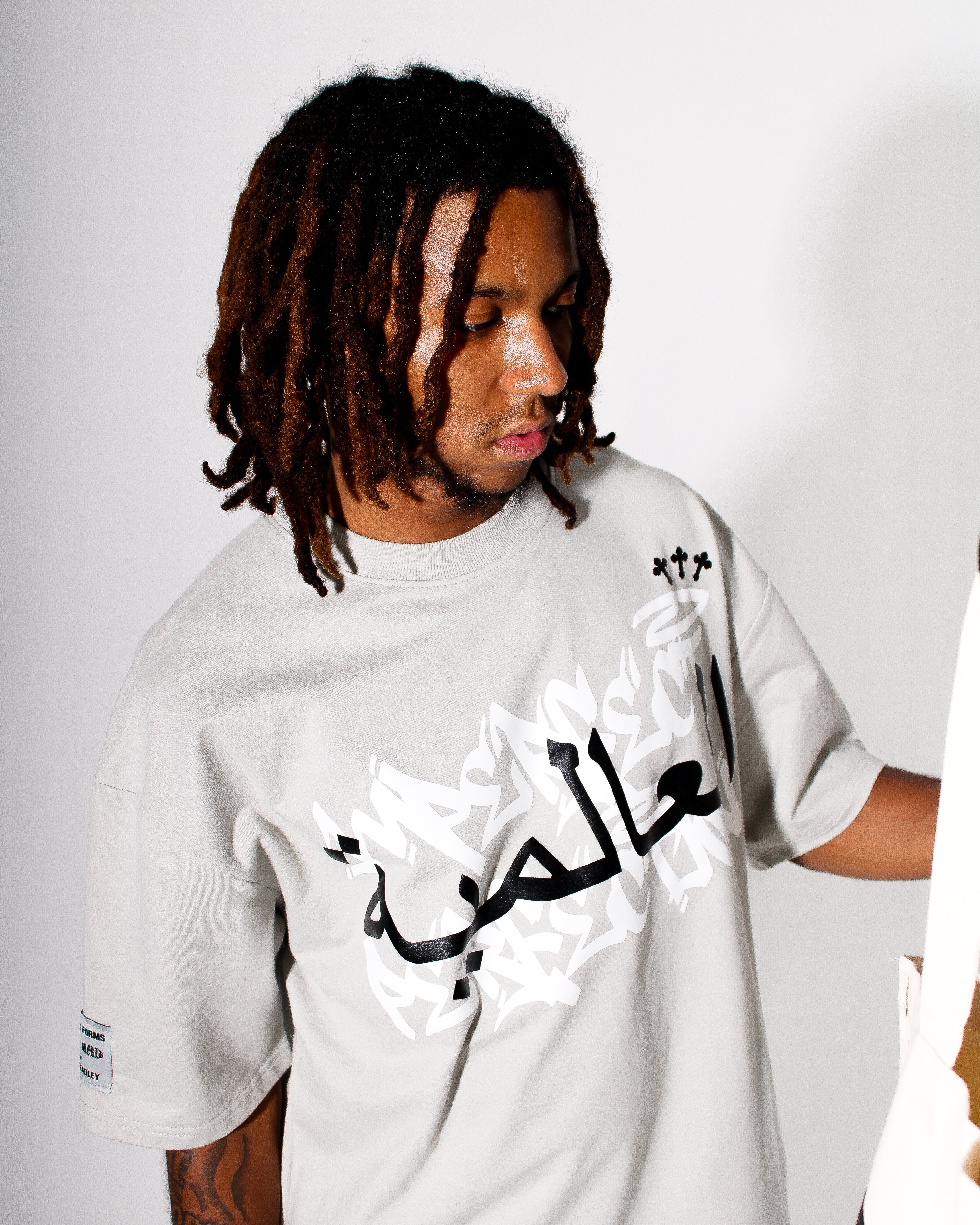 Person wearing a grey t-shirt with Arabic text on a plain background