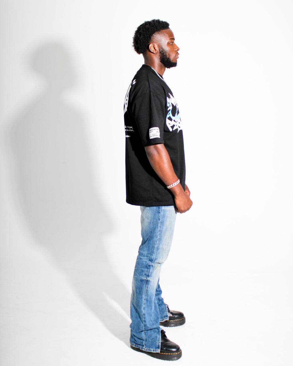 Man wearing a black t-shirt with a graphic design and light blue jeans against a white background