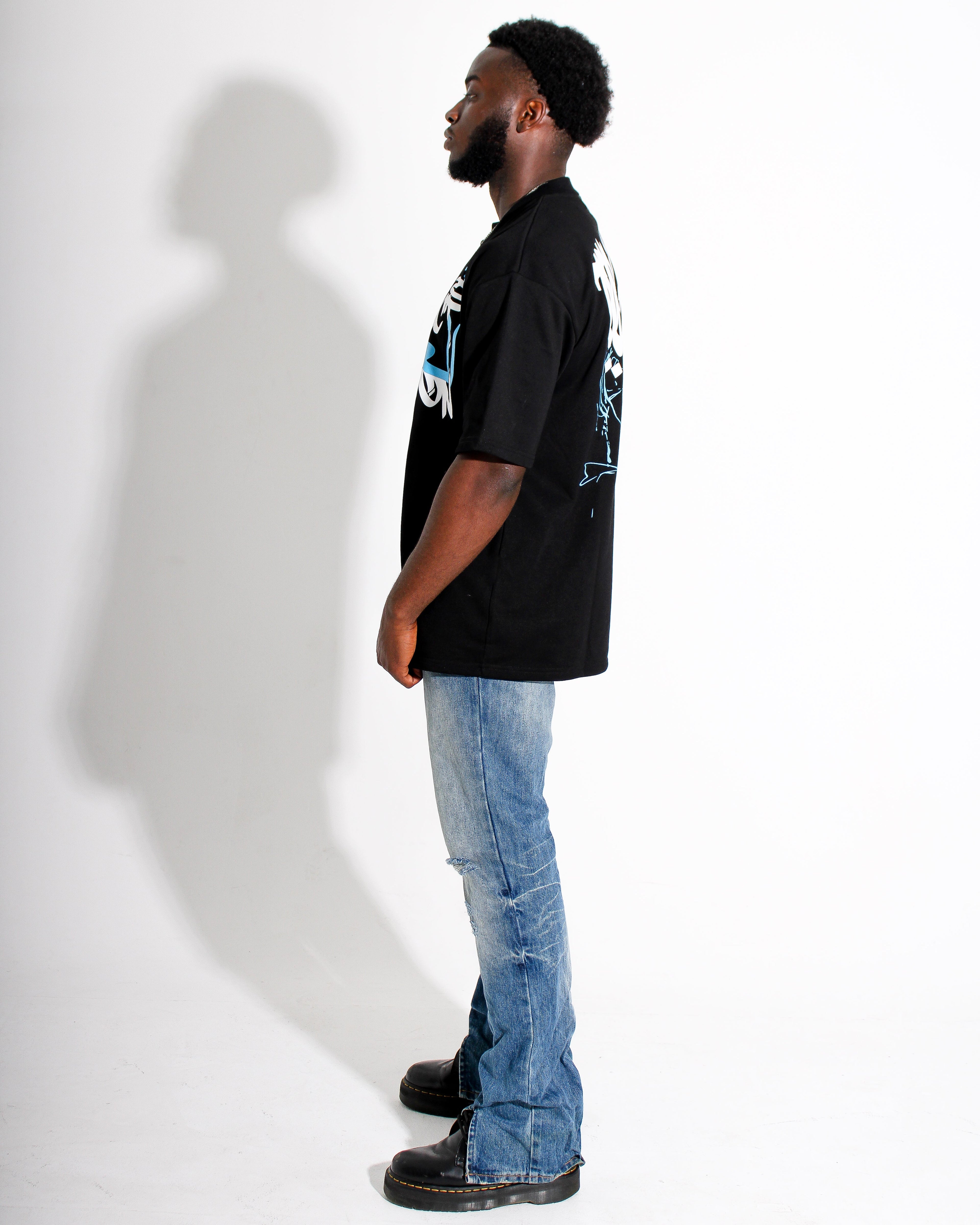 Man wearing a black t-shirt with a graphic design and blue jeans standing against a white background