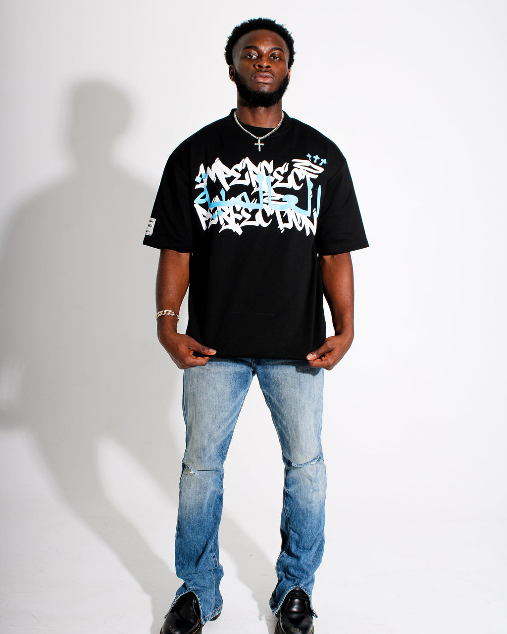 Person wearing a black t-shirt with white text and blue jeans on a white background