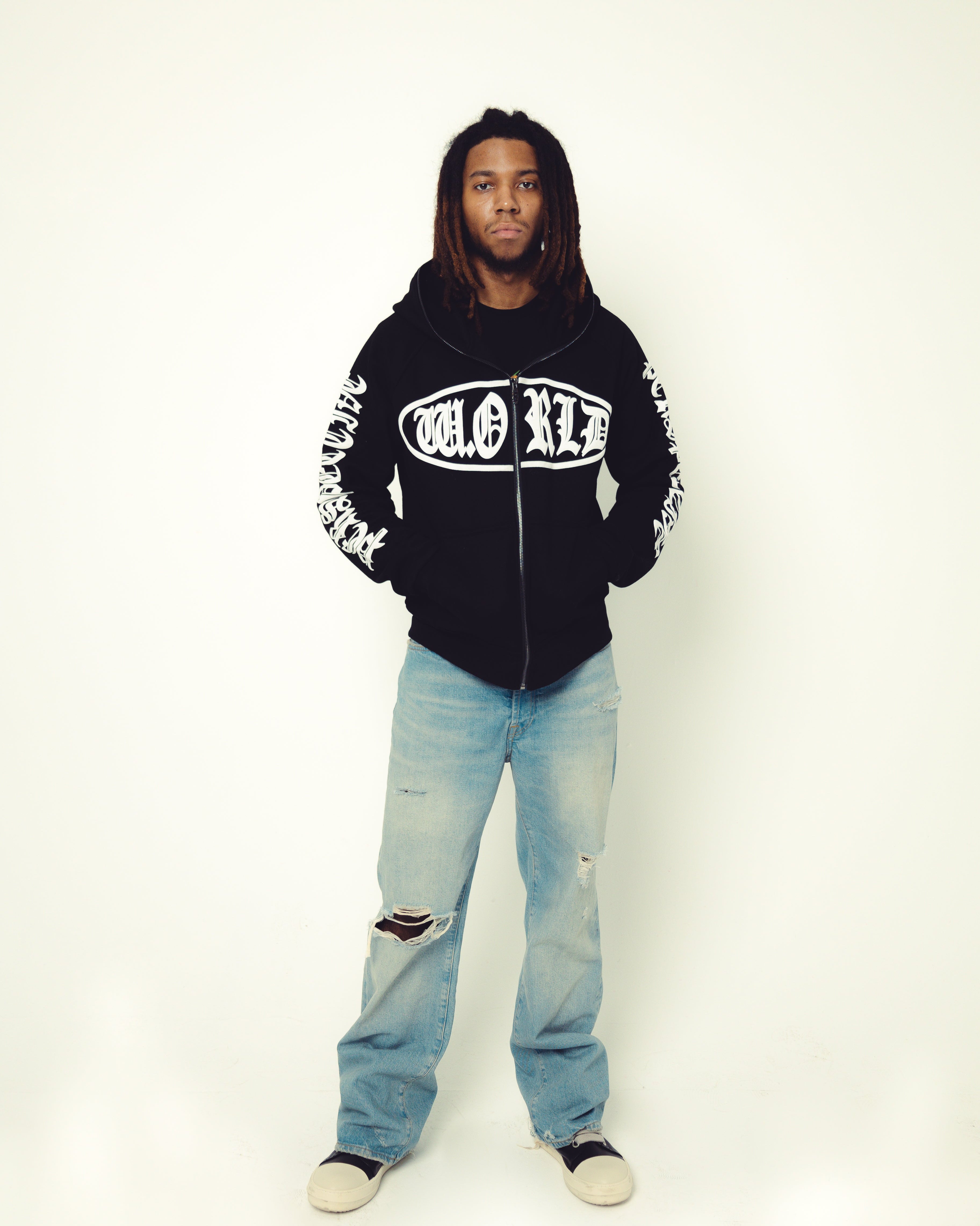 Person wearing a black hoodie with white text and light blue jeans on a white background