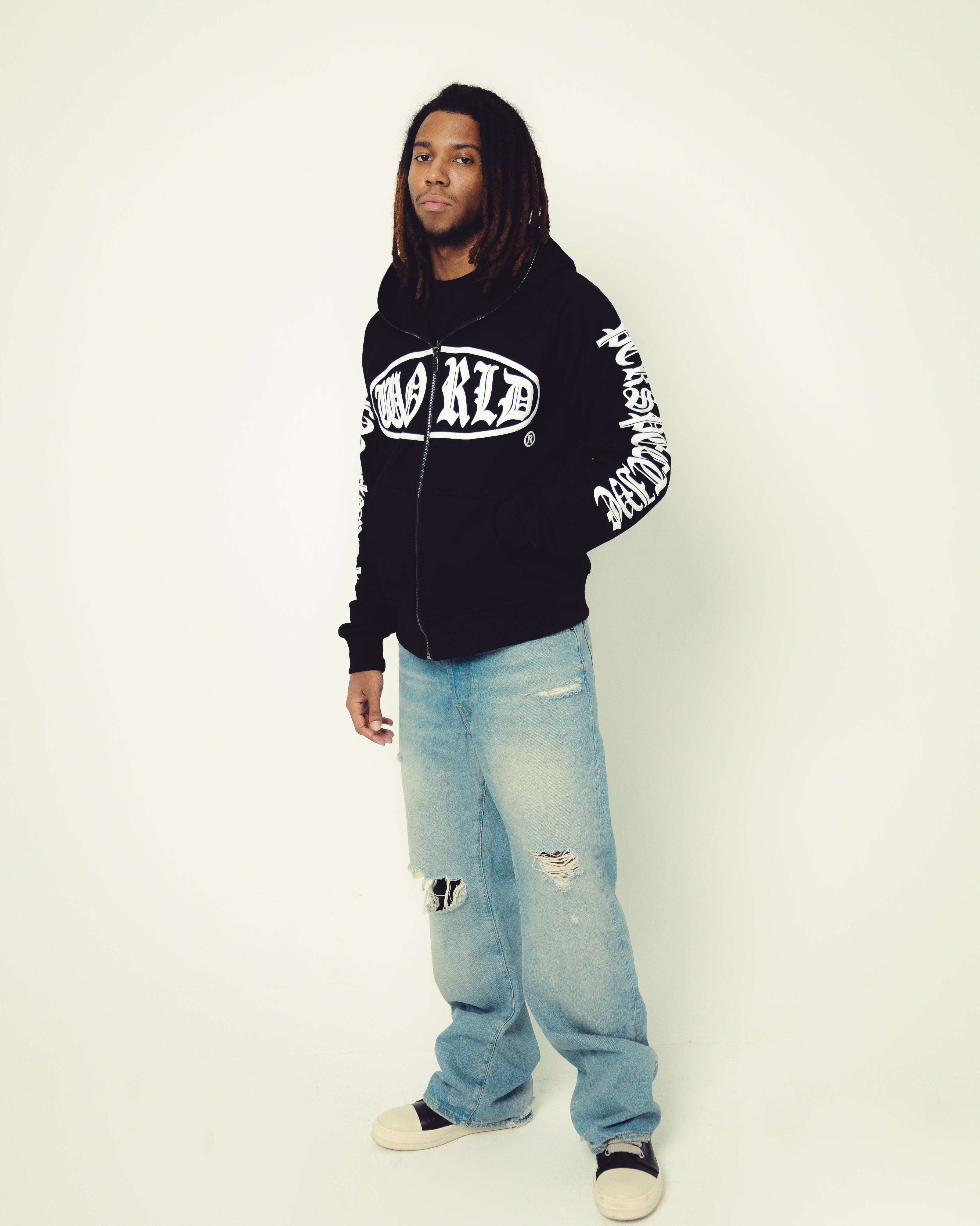 Person wearing a black hoodie with white text and light blue jeans on a white background