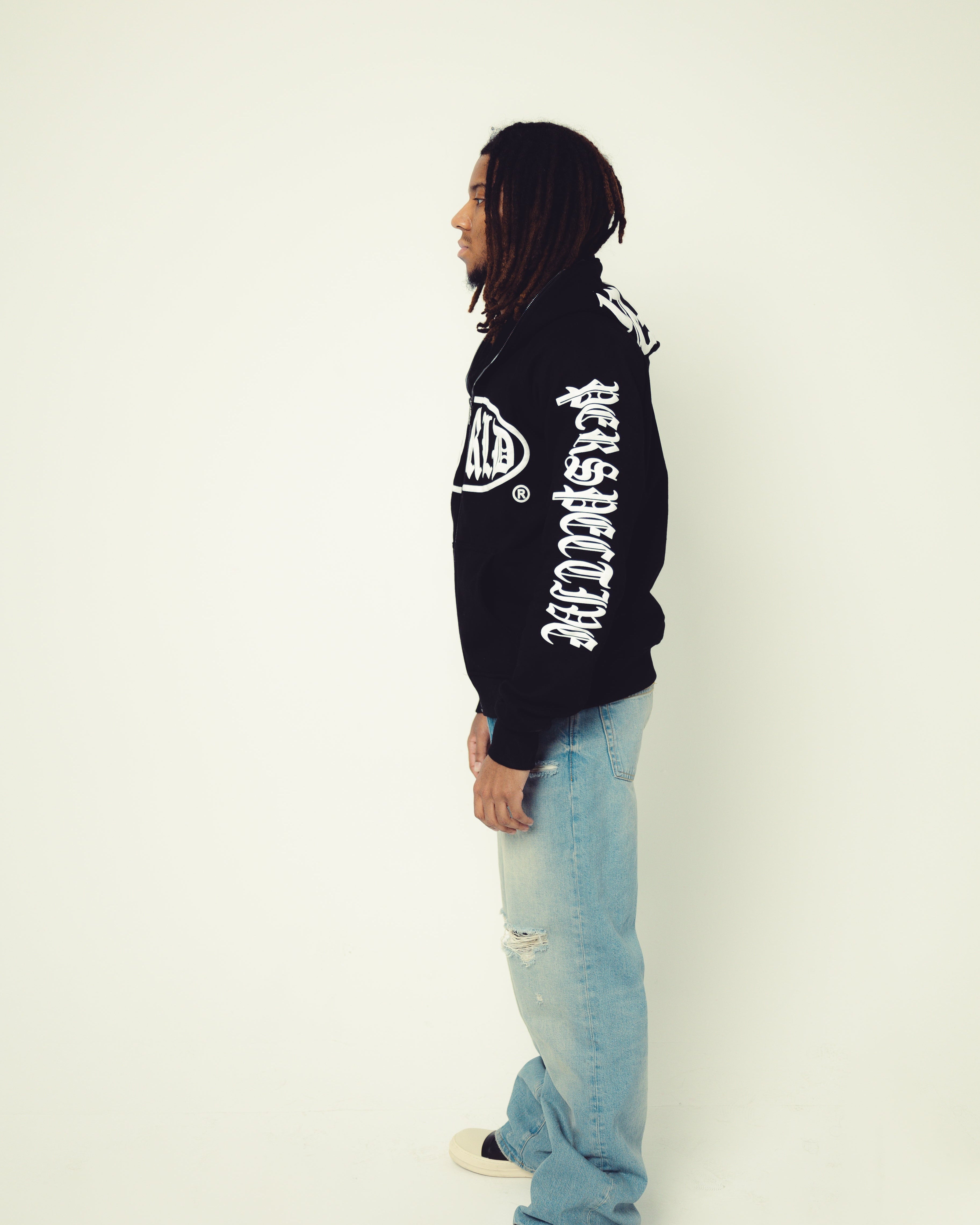 Person wearing a black hoodie with white text and light blue jeans on a white background