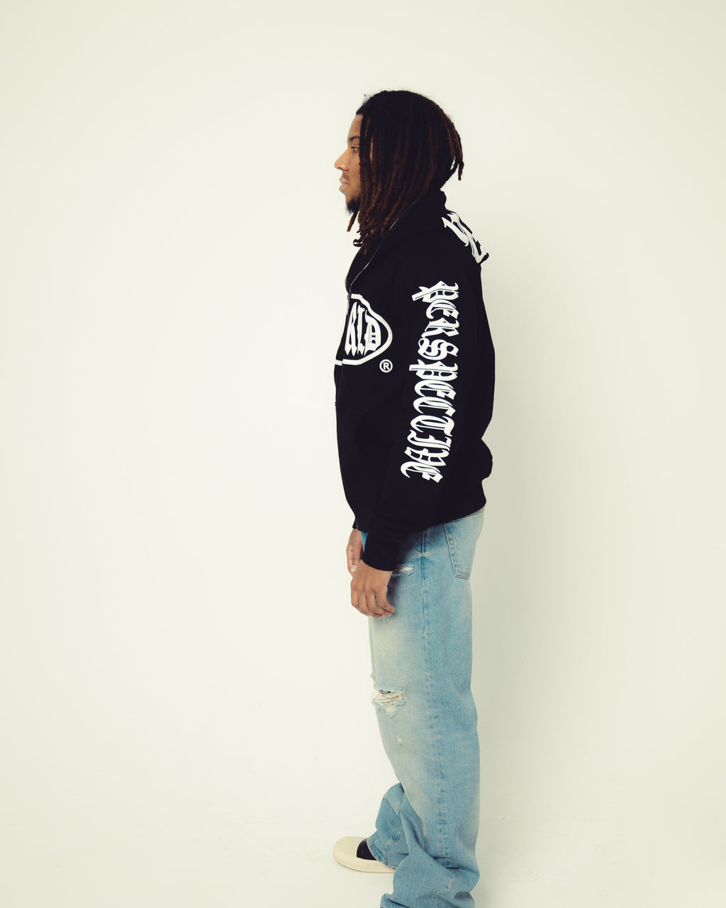 Person wearing a black hoodie with white text and light blue jeans on a white background