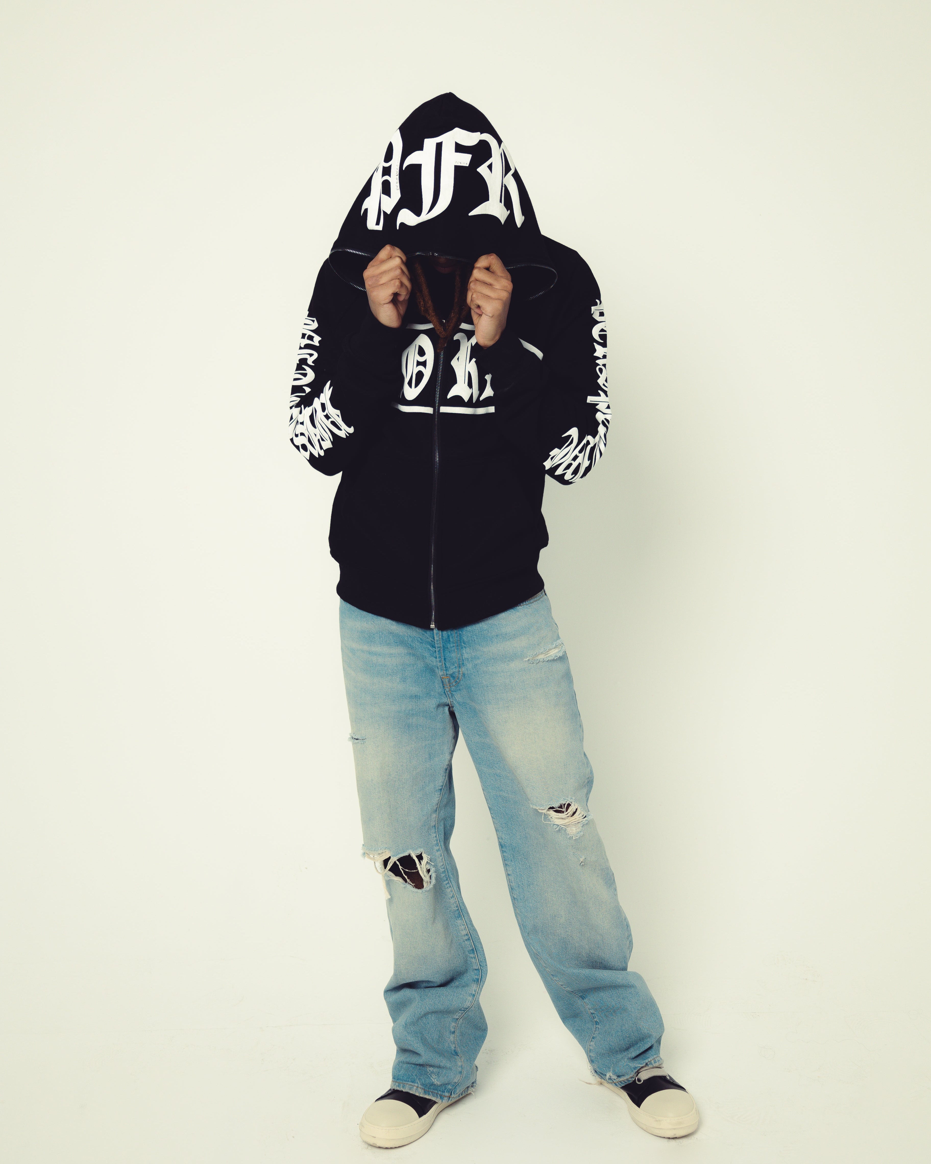 Person wearing a black hoodie with white text and light blue jeans on a white background