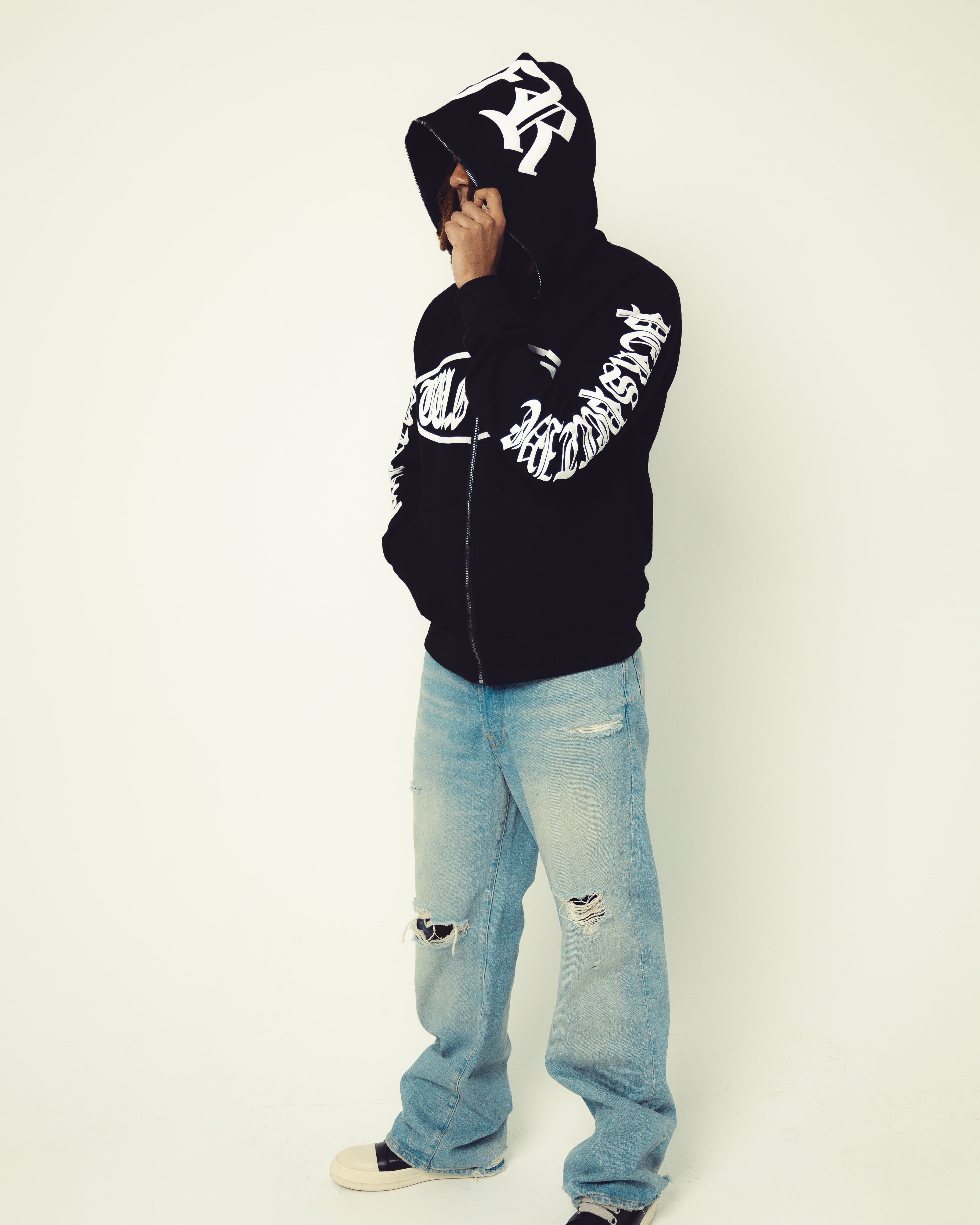 Person wearing a black hoodie with white text and light blue jeans on a white background