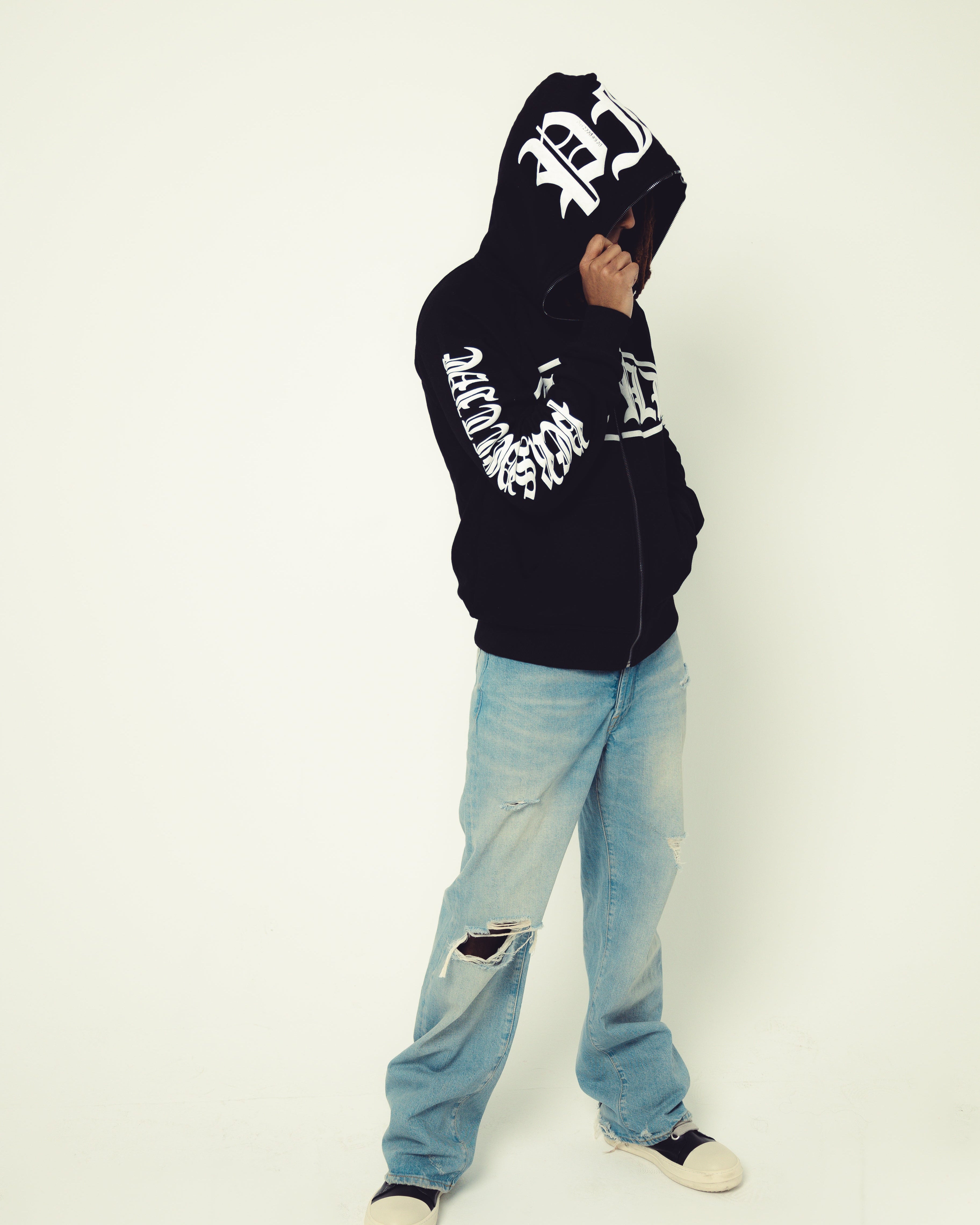 Person wearing a black hoodie with white text and light blue jeans on a white background