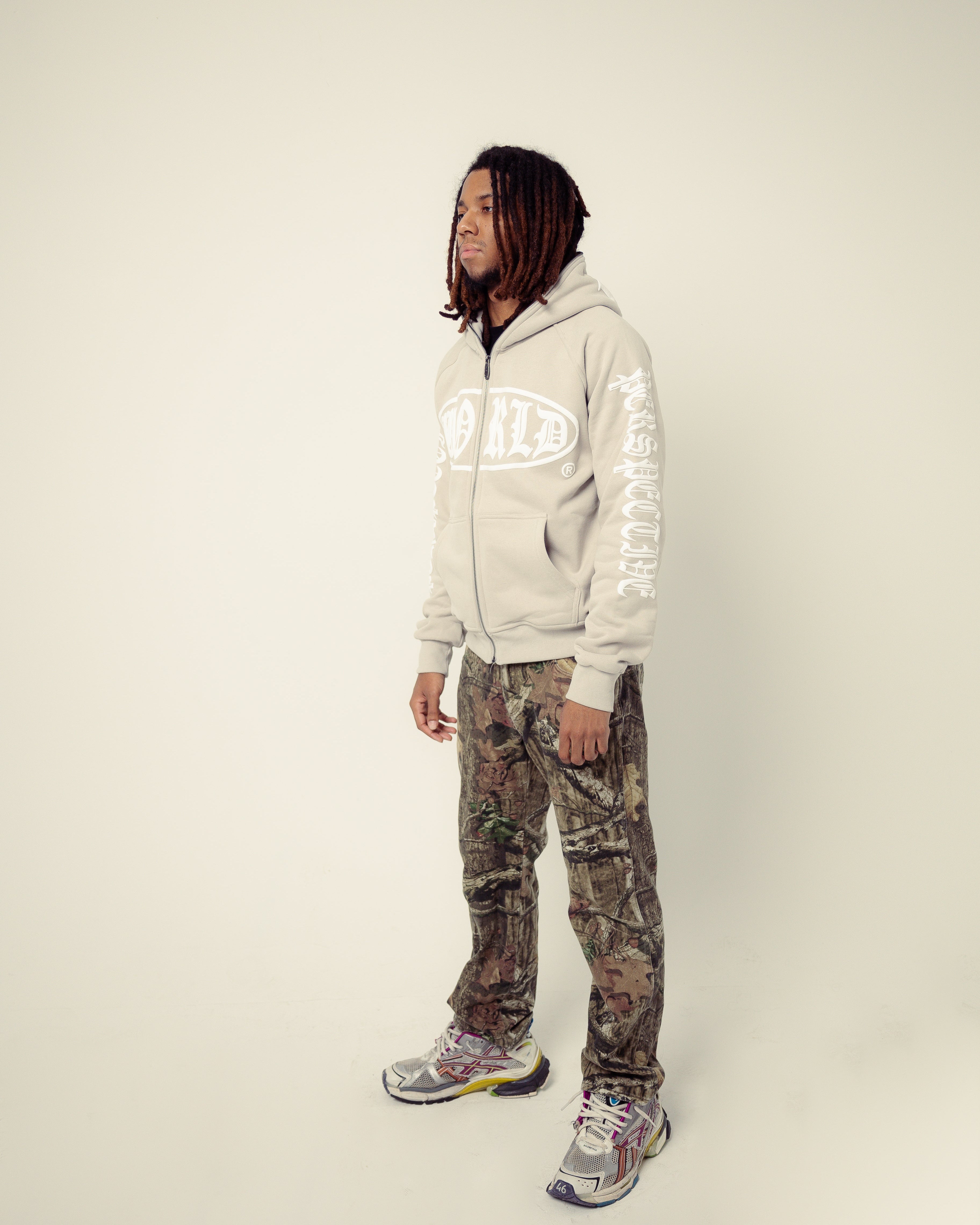 Person wearing a light gray hoodie with text and camouflage pants on a white background