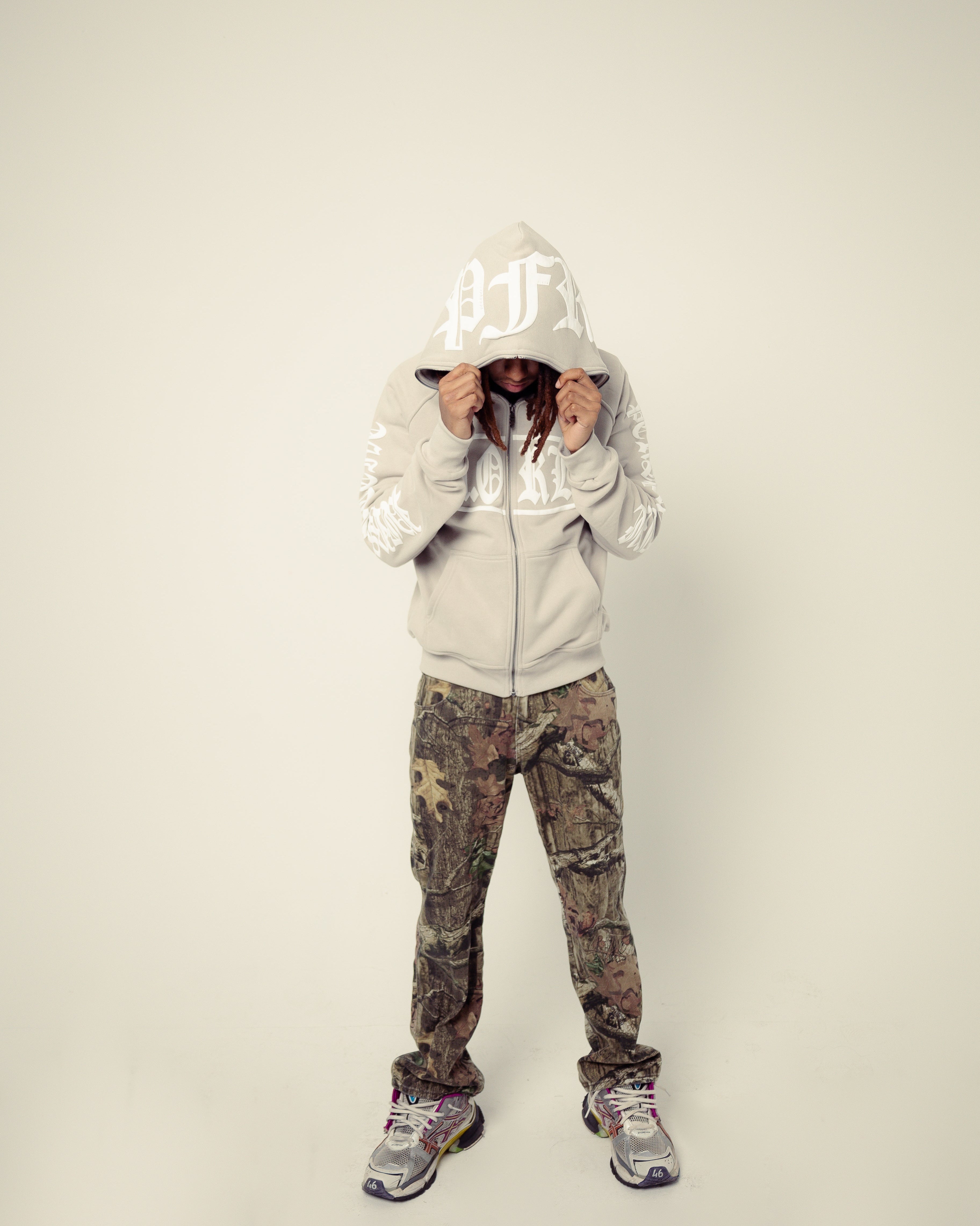 Person wearing a white hoodie and camouflage pants on a plain background