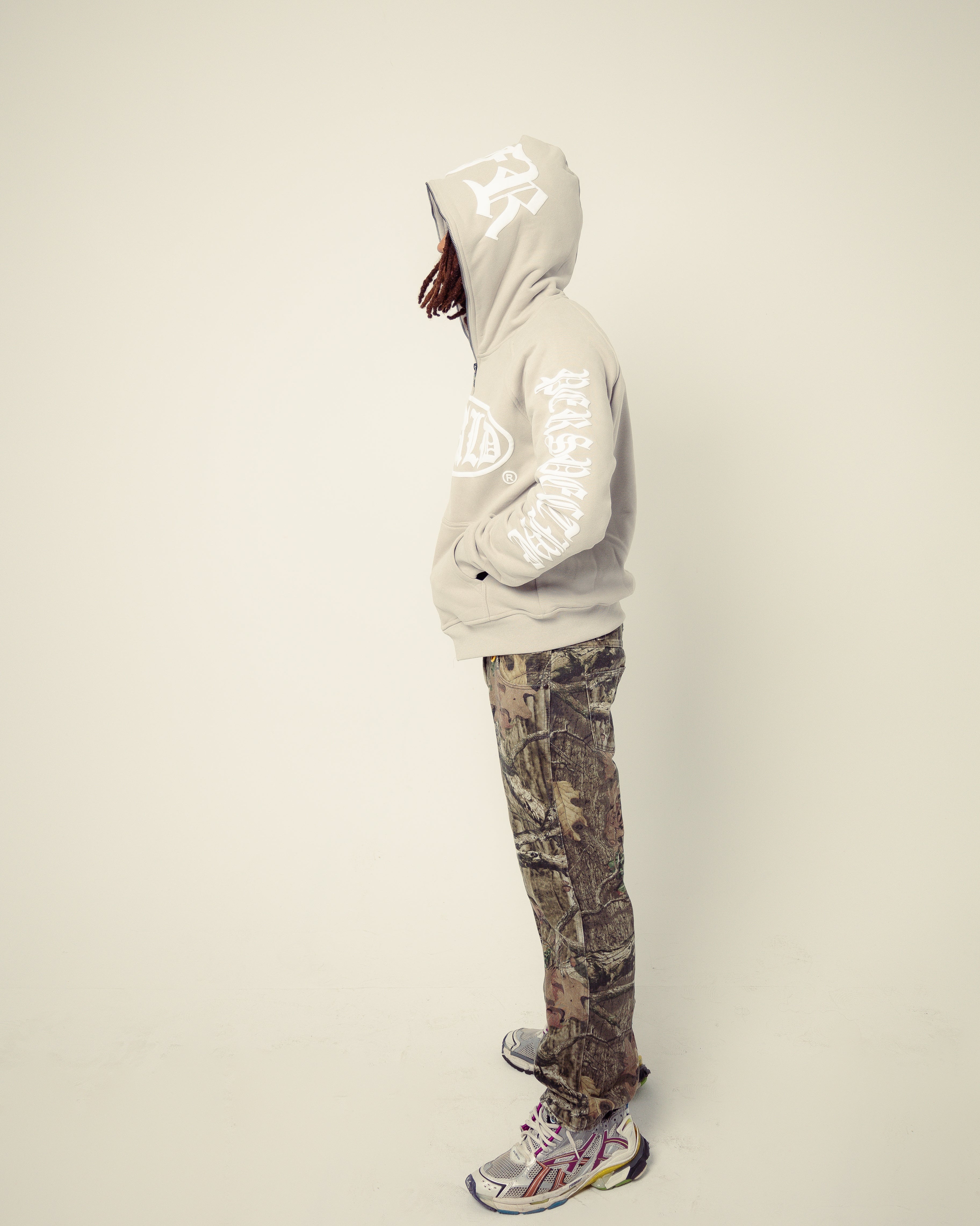 Person wearing a reflective hoodie and camouflage pants on a plain background