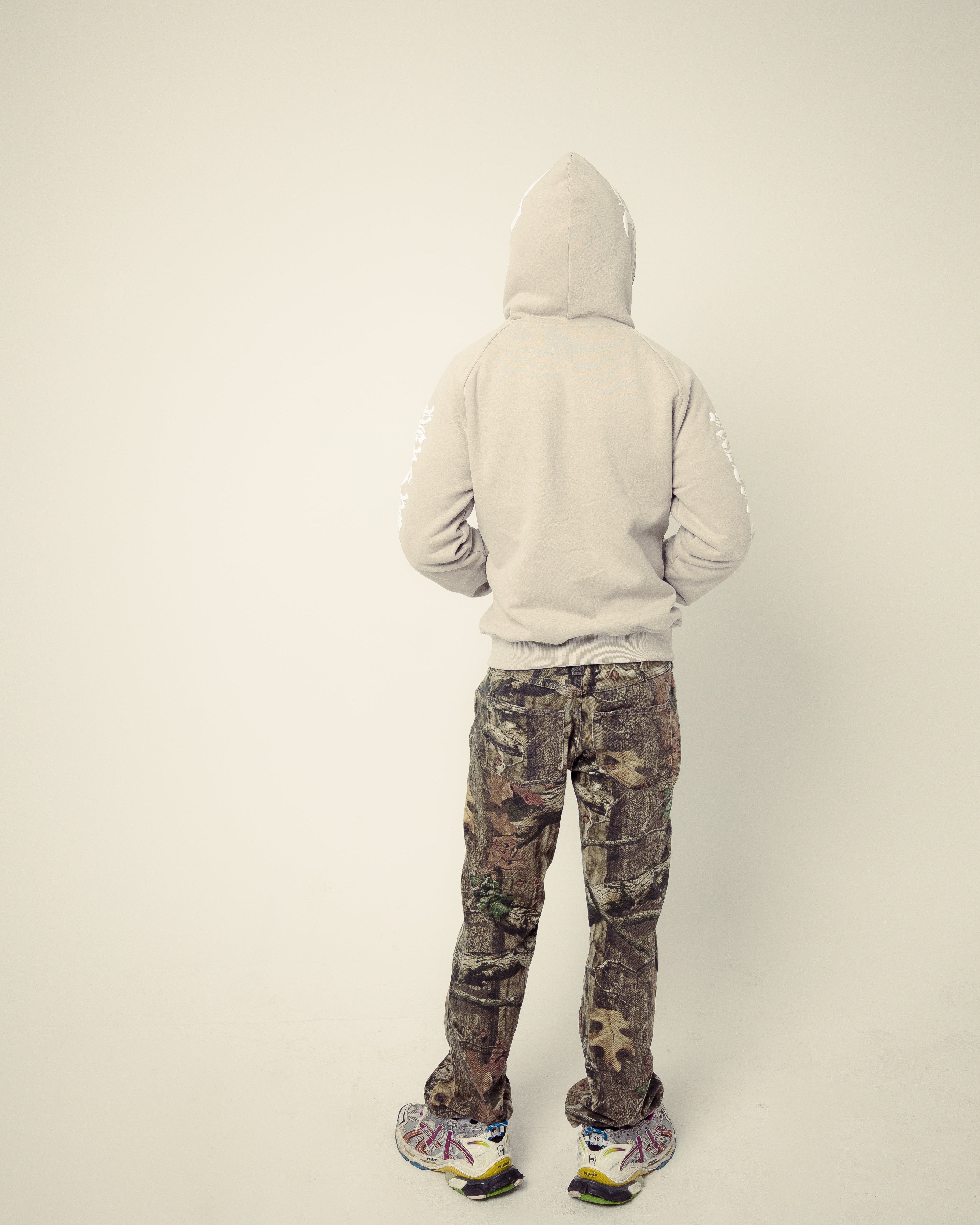 Person wearing a light gray hoodie and camouflage pants on a plain background