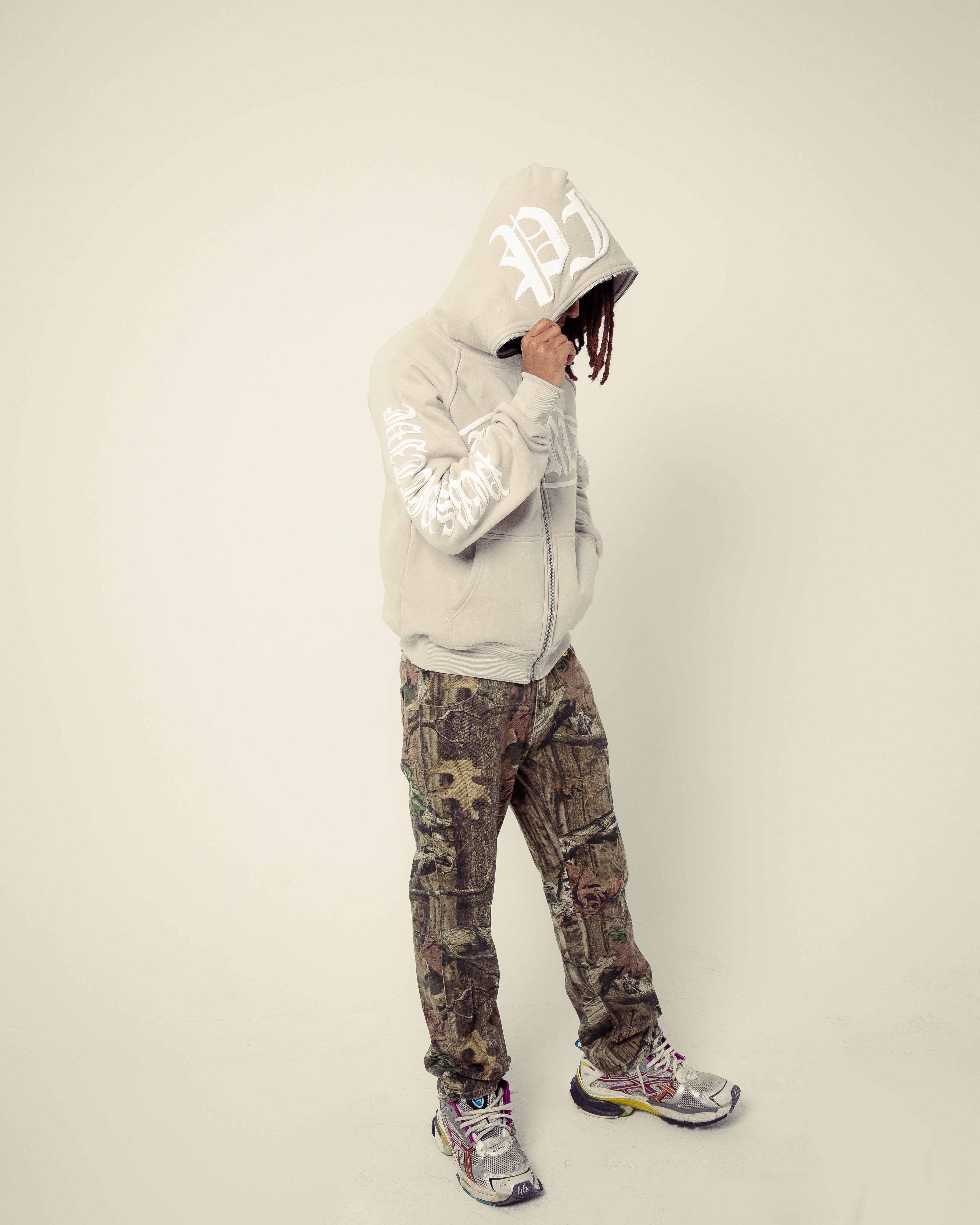 Person wearing a reflective hoodie and camouflage pants on a plain background
