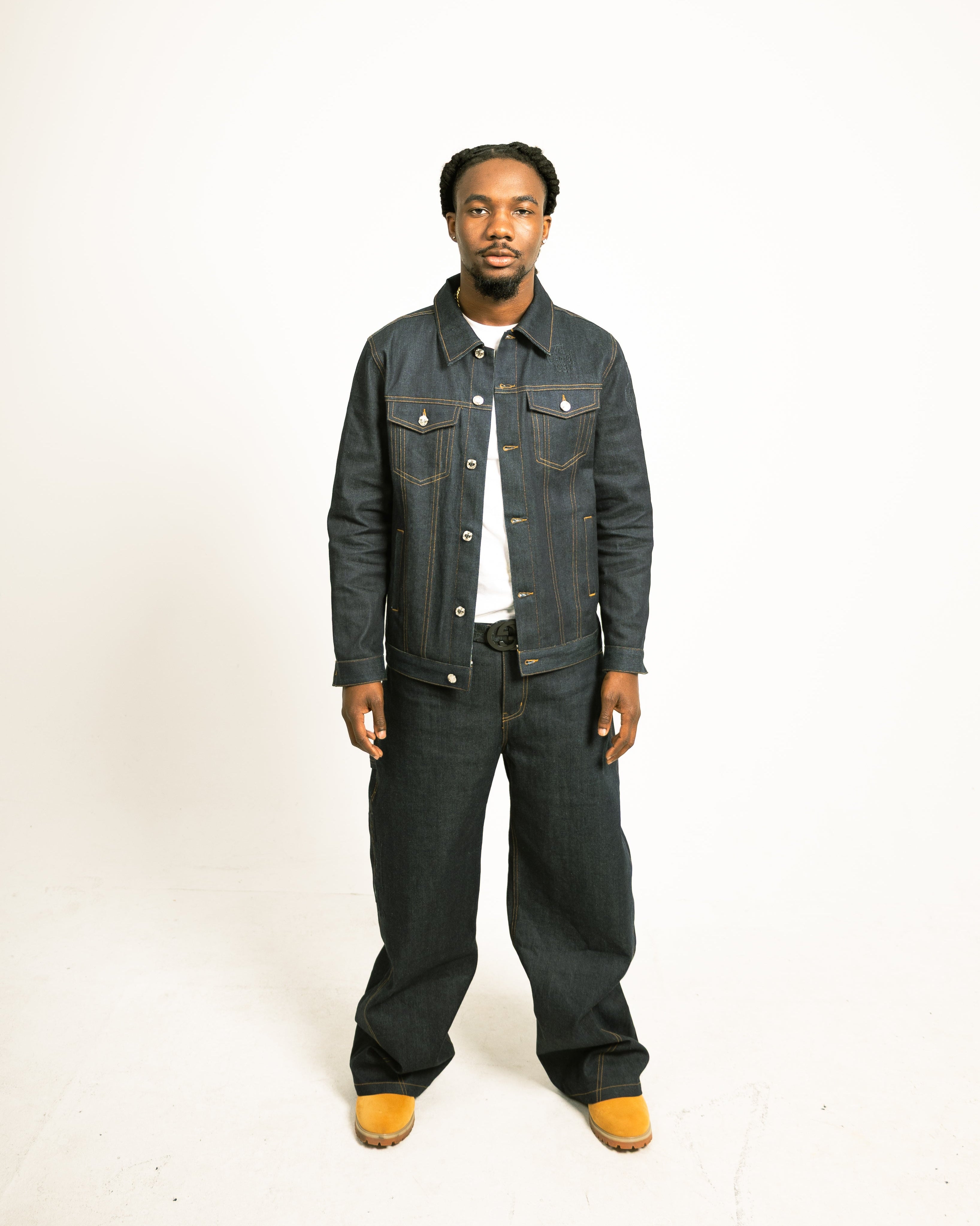 Person wearing a dark denim jacket and pants on a white background