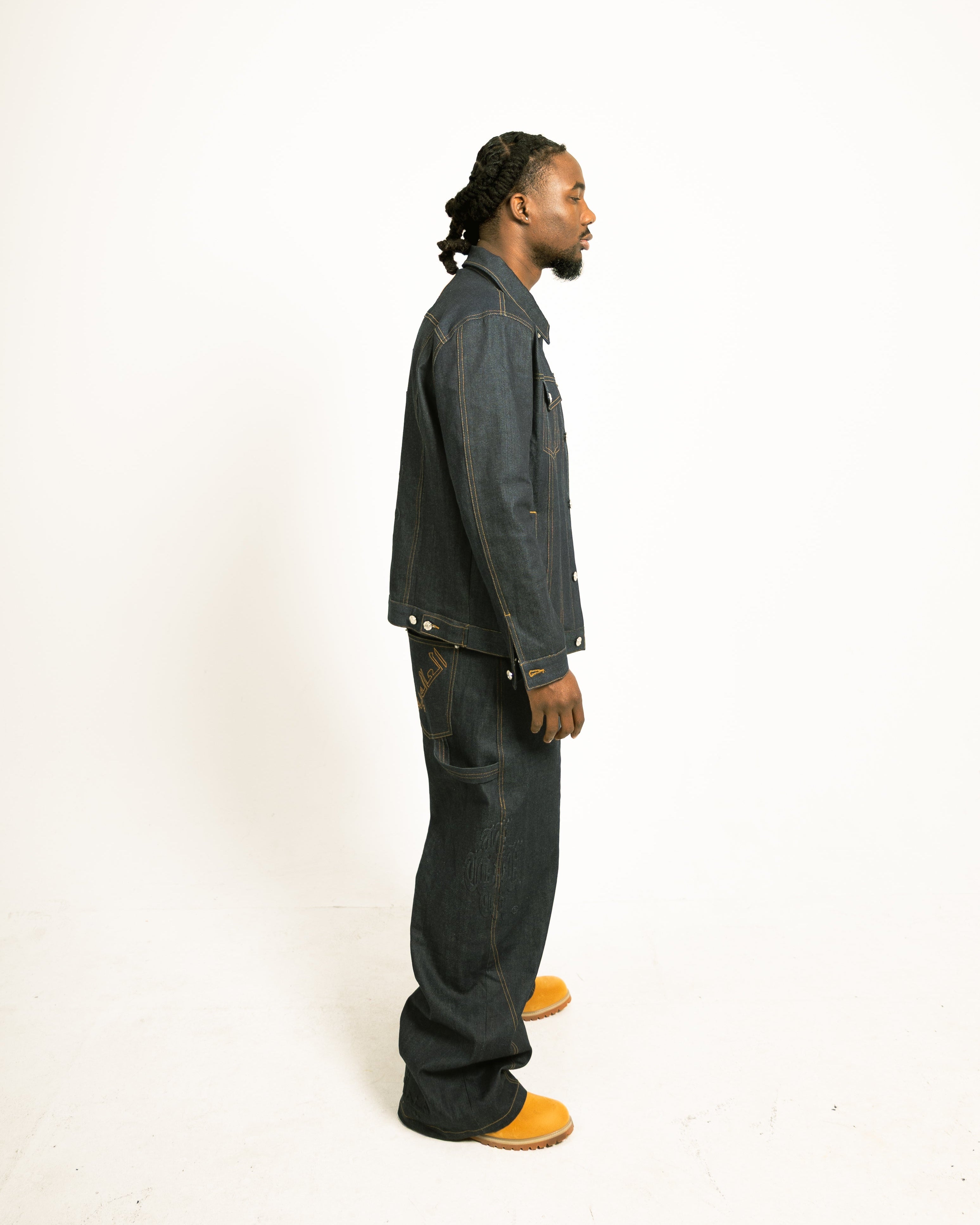 Man wearing a dark denim jacket and pants on a white background