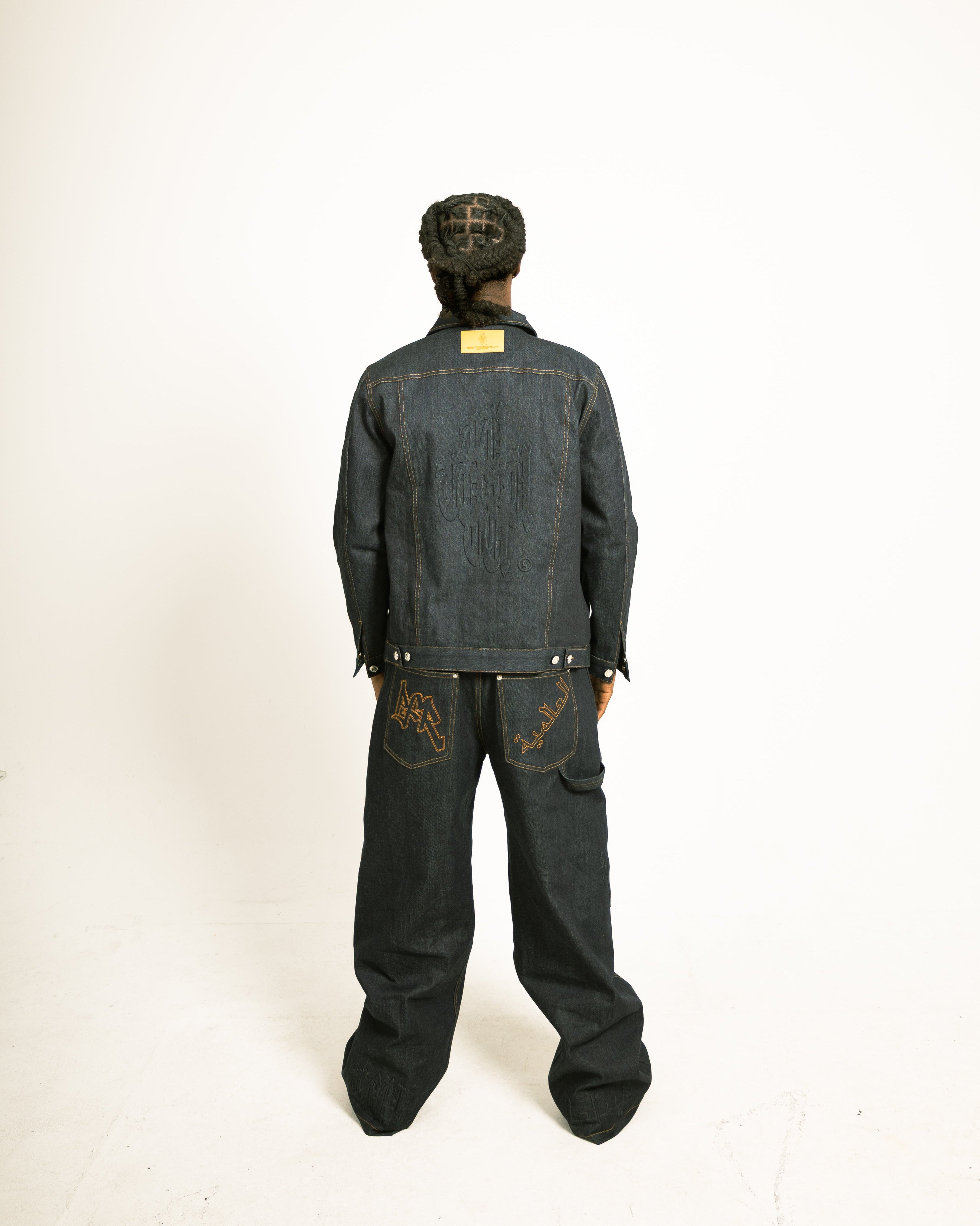 Person wearing a dark denim jacket and pants on a white background