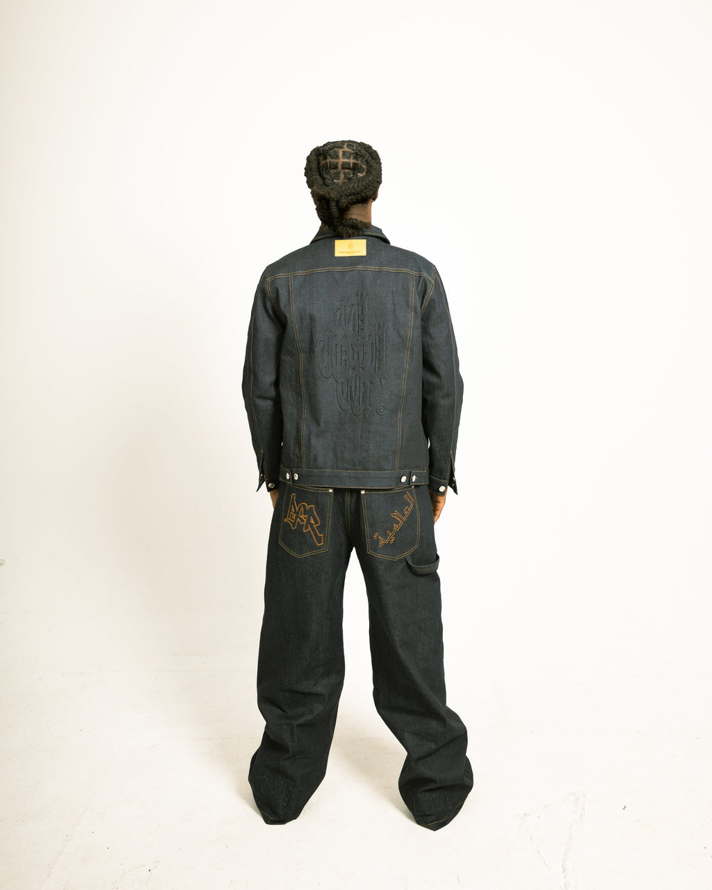 Person wearing a dark denim jacket and pants on a white background