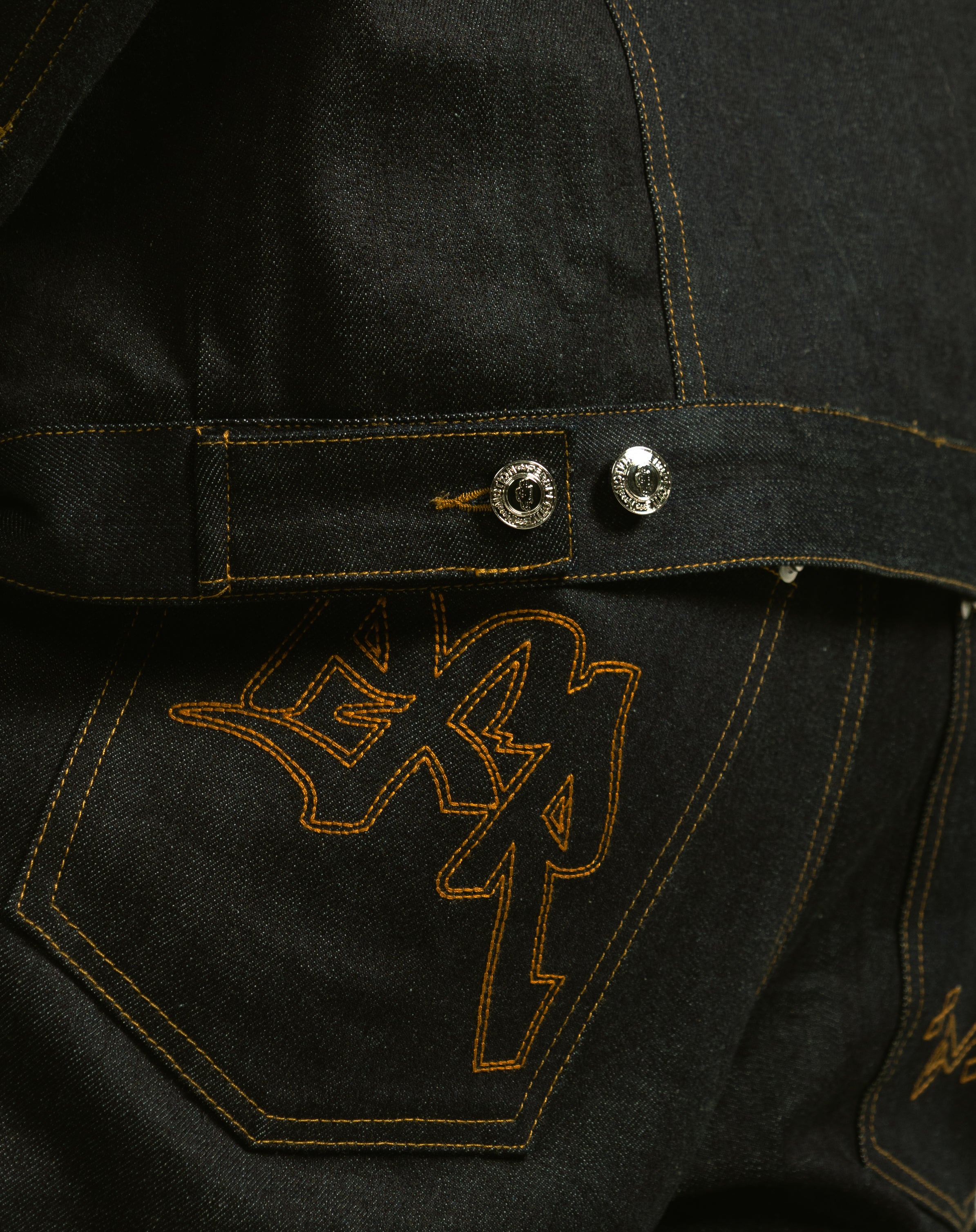 Close-up of a dark denim jacket with embroidered logo on the chest pocket.
