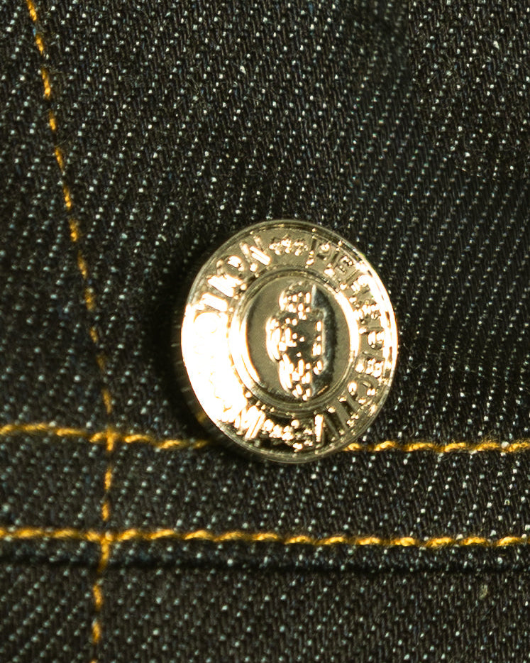 Close-up of a gold button on black denim fabric with yellow stitching.