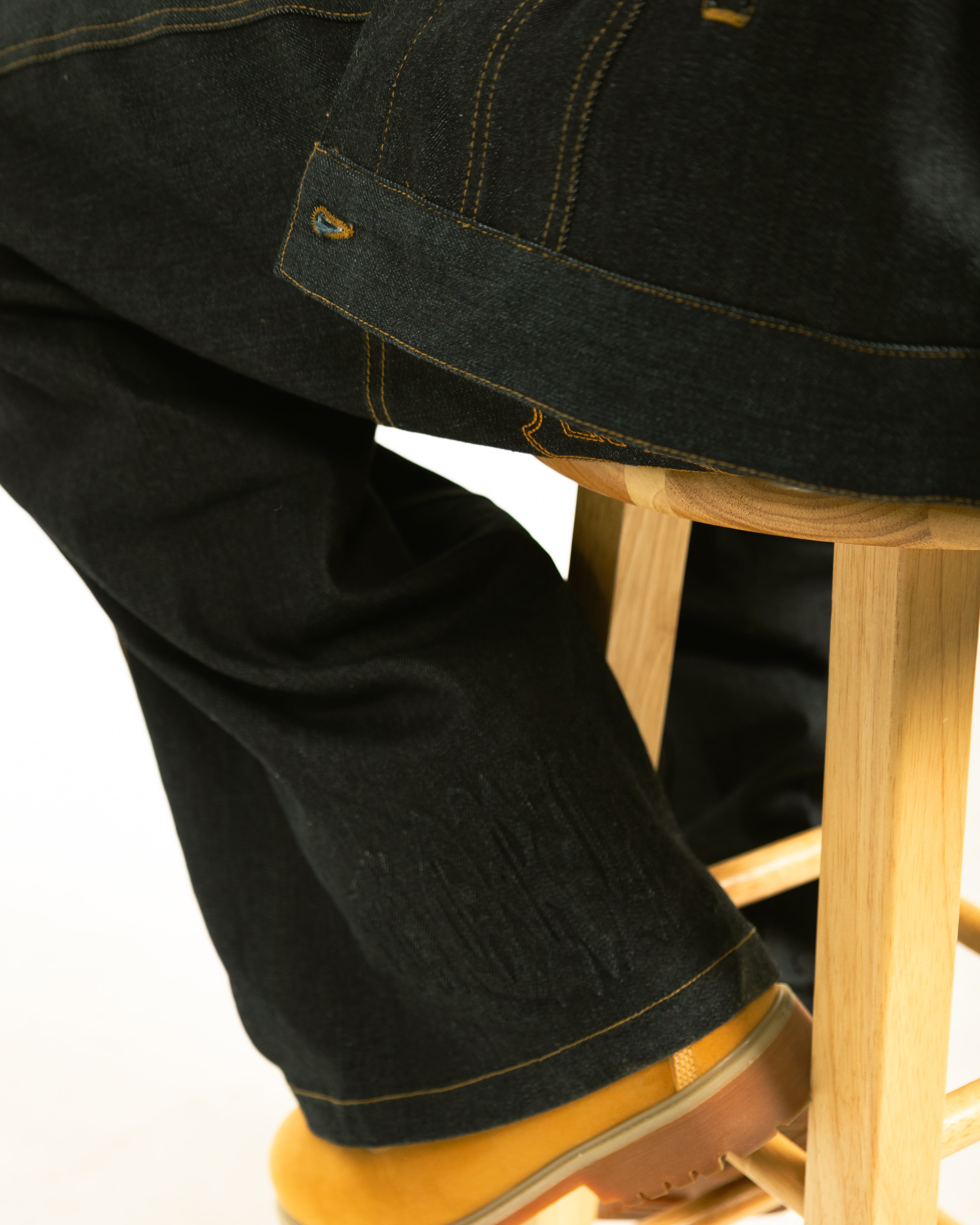 Person wearing black jeans and yellow boots sitting on a wooden stool.